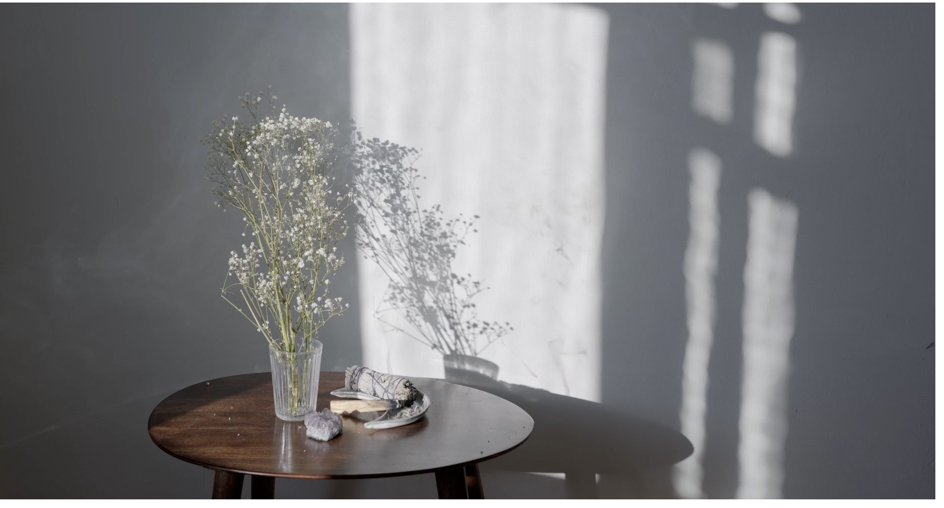 A small wooden table with a glass of baby's breath in soft window light